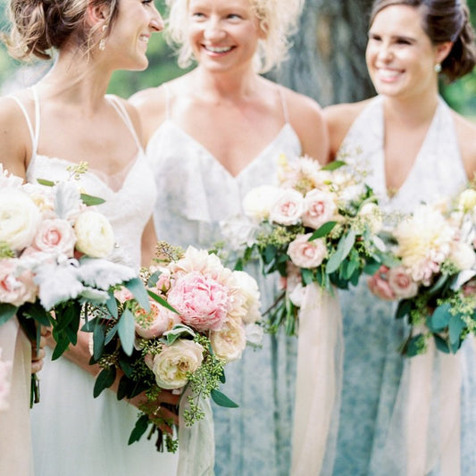 Two bridesmaids and a bride holding bouqiets of pink peonies and white roses