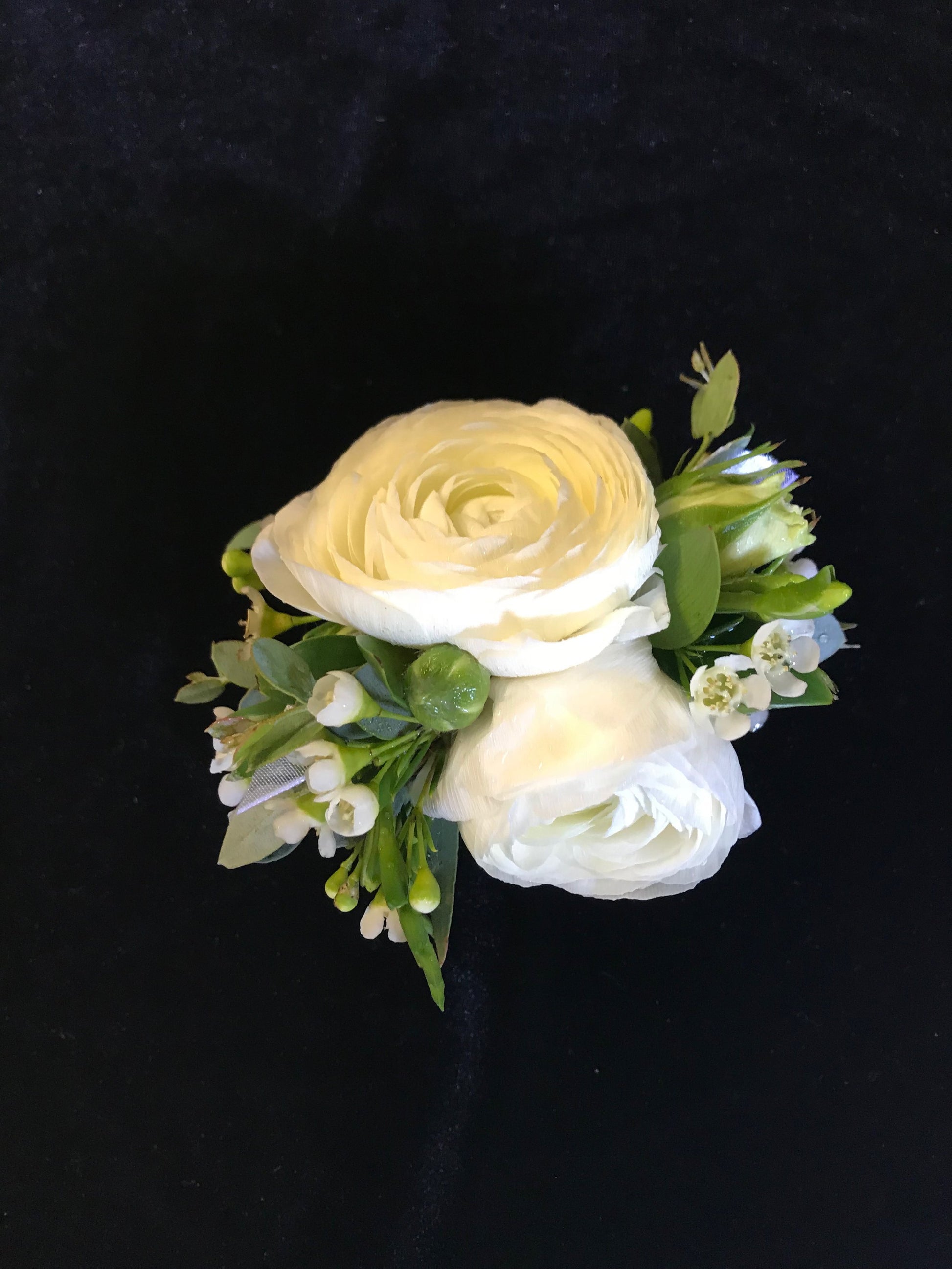 Floral corsage with white roses and greenery on a black background