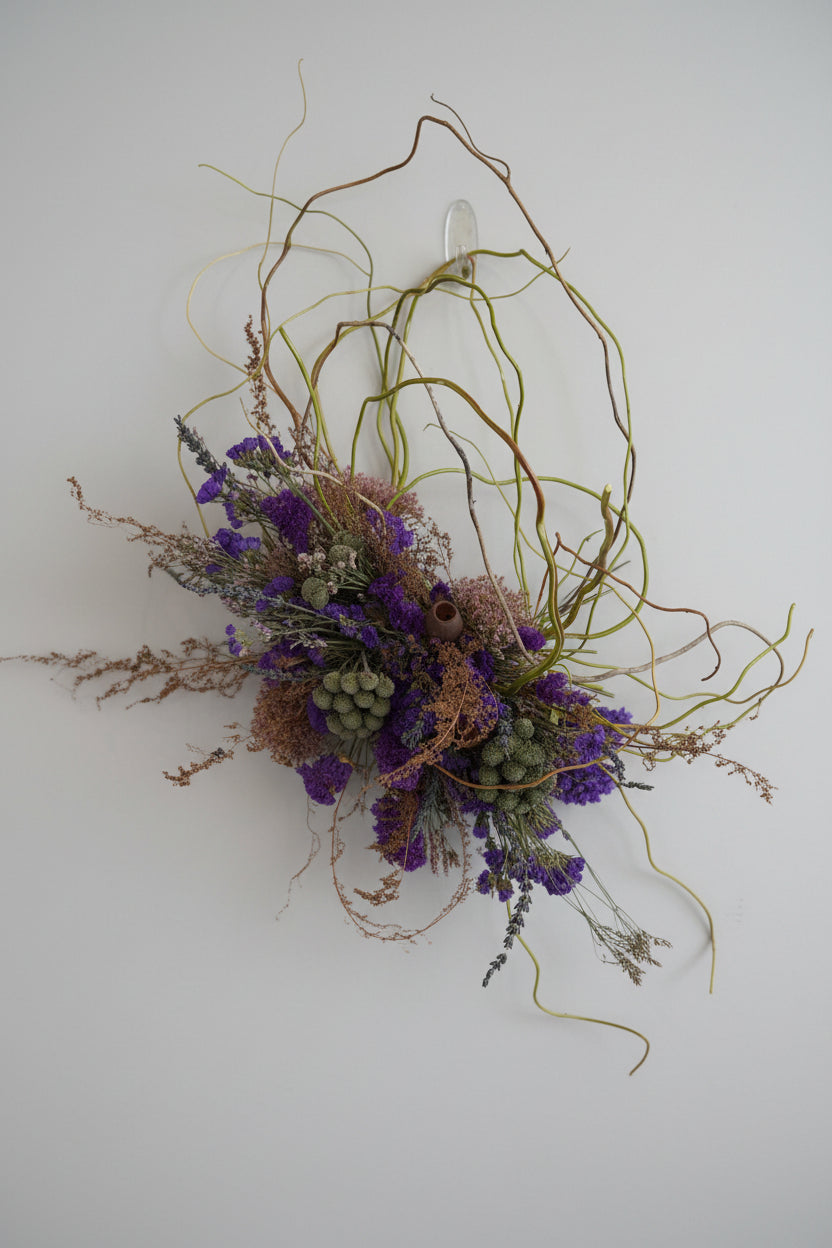 Decorative wreath with purple flowers and greenery against a white brick wall.