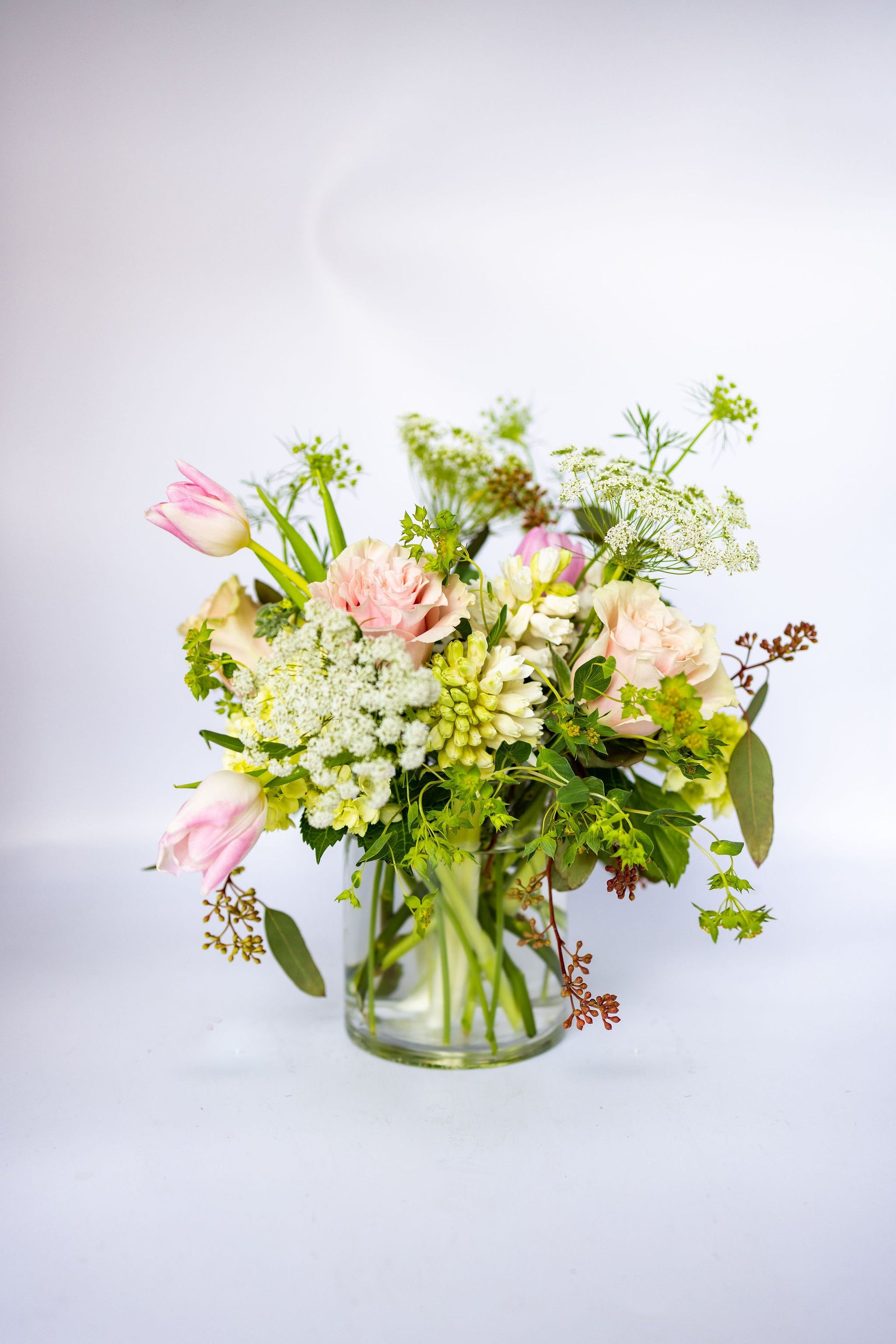 Bouquet of blush and white flowers in a clear vase on a light background