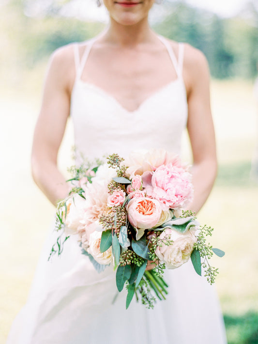 Bride holding a bouquet of flowers in light blushes, lights peaches, and creamy whites