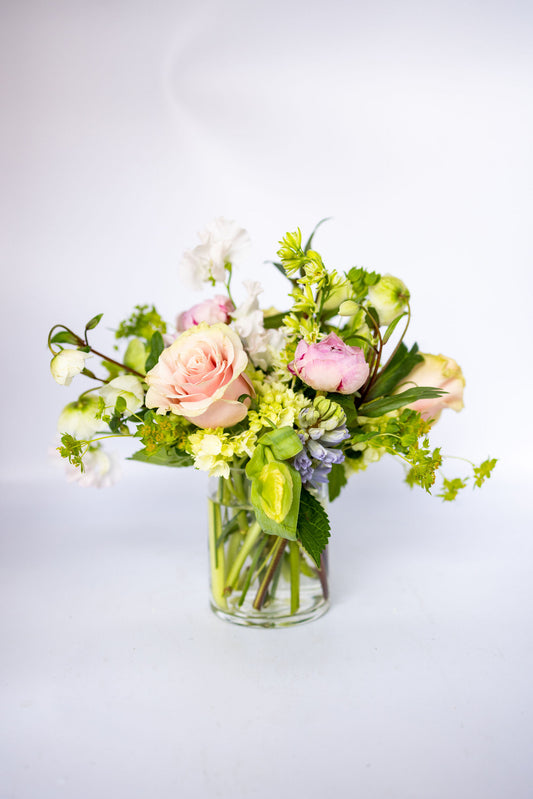 Bouquet of blush, peach, and white flowers in a clear vase on a light gray background