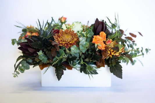 Floral arrangement with autumn colors in a white flower box on a light background