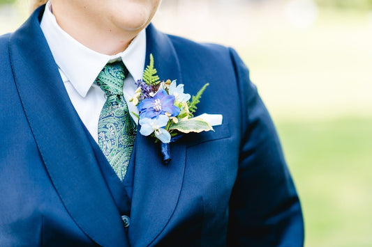 Person wearing a blue suit with a blue floral boutonniere and green tie.