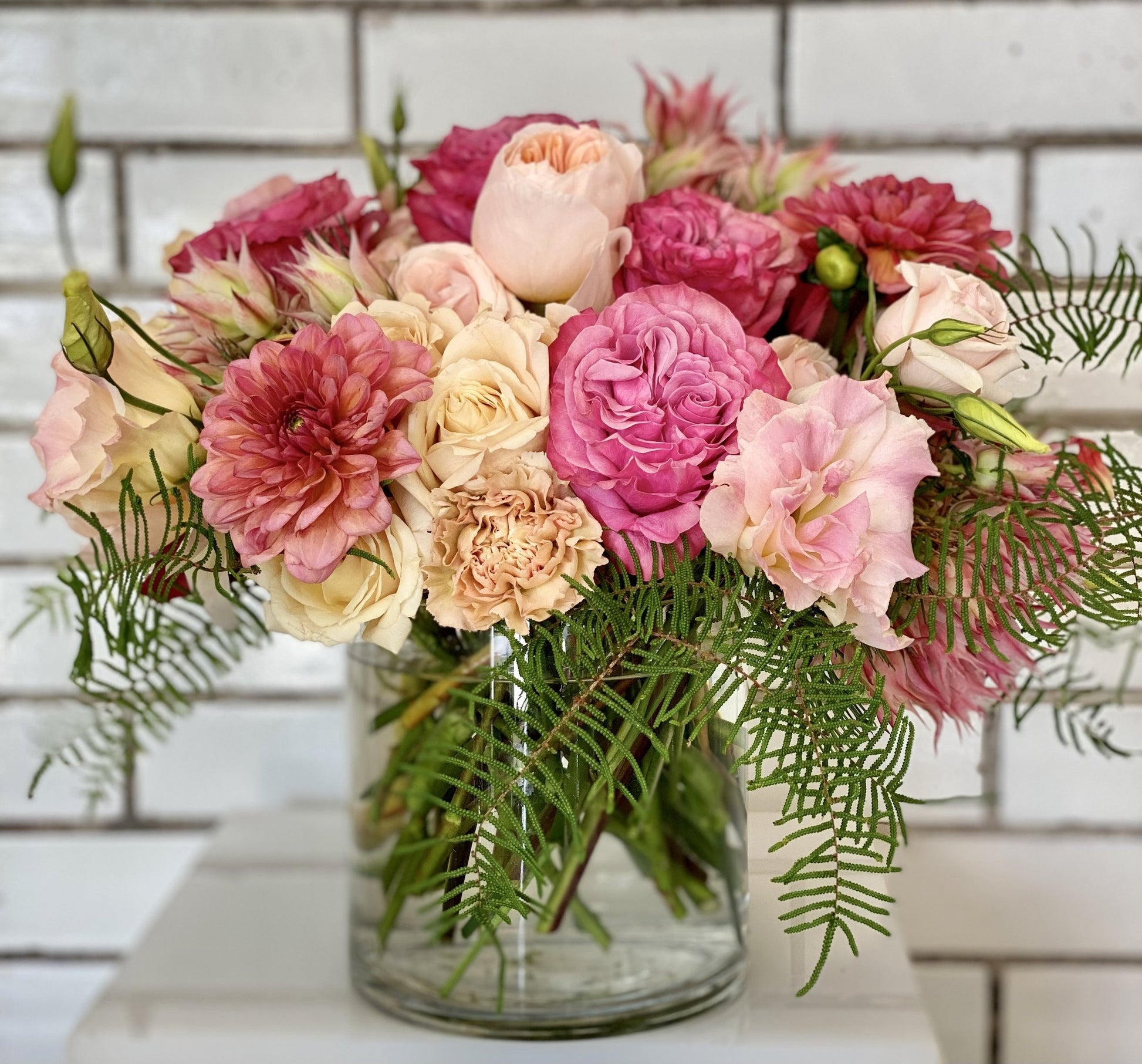 Bouquet of pink, blush, and cream flowers in a clear vase on a light background