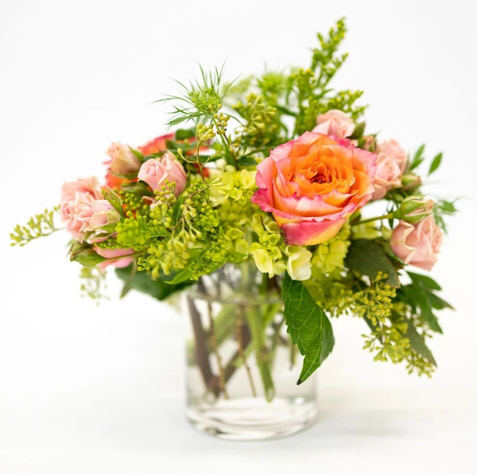 Bouquet of pink, orange, and bright green flowers in a clear vase on a white background
