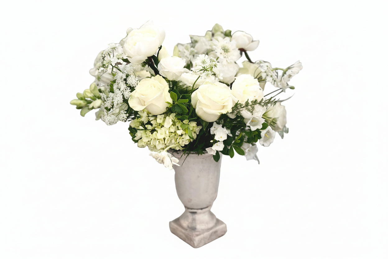 Bouquet of white flowers in a stone vase against a white brick wall.