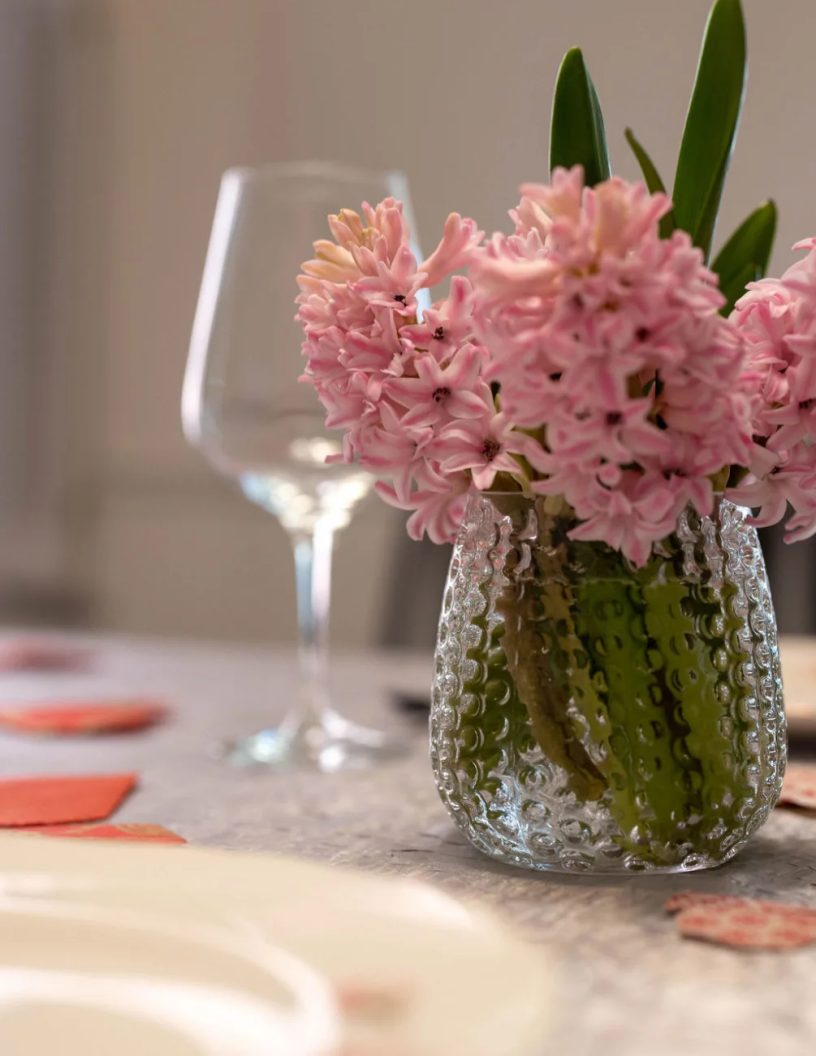 Pink flowers in a cleartextured glass vase on a table with a blurred background