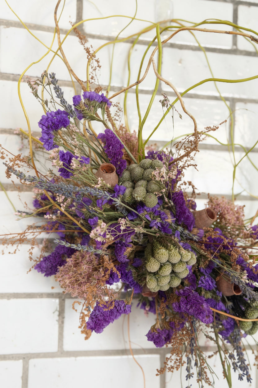 Dried floral arrangement with purple and green elements on a textured wall background