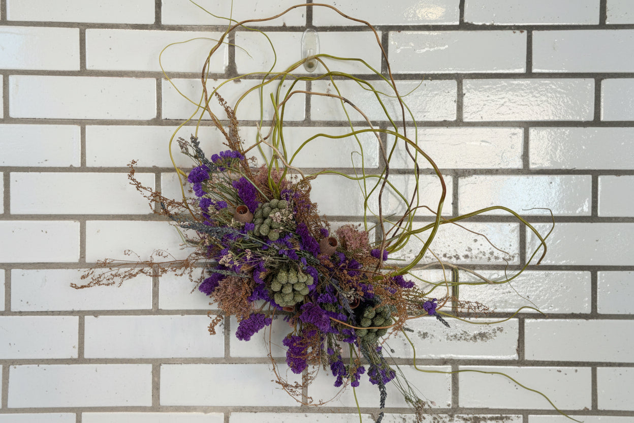 Dried floral arrangement with purple and green elements against a tiled wall.