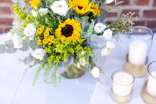 Bouquet of sunflowers and white flowers with candles on a table.