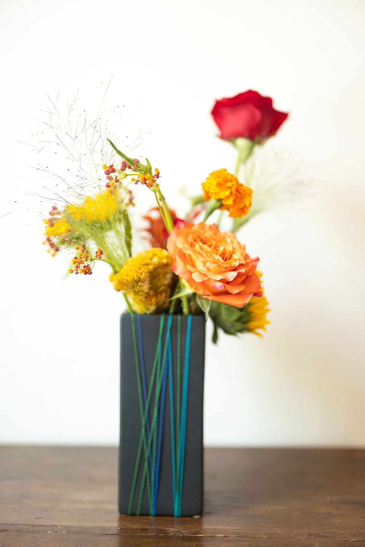 Gray stone vase with red, yellow, and orange flowers on a wooden surface