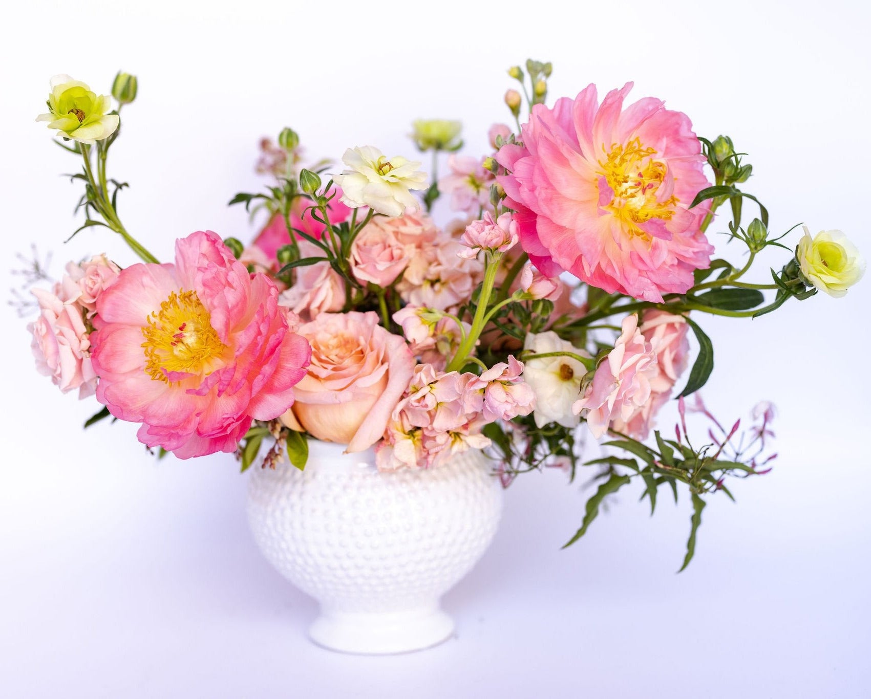 Bouquet of pink, peach, and white flowers in a white vase on a light background