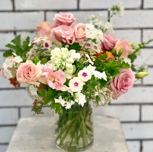 Bouquet of light pink and white flowers in a clear vase against a tiled wall background