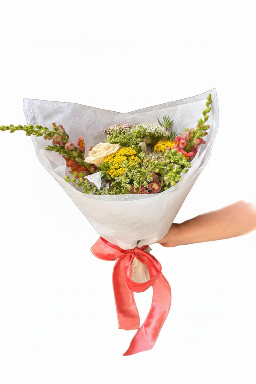 Bouquet of flowers wrapped in cellophane with a pink ribbon held by a hand on a white background
